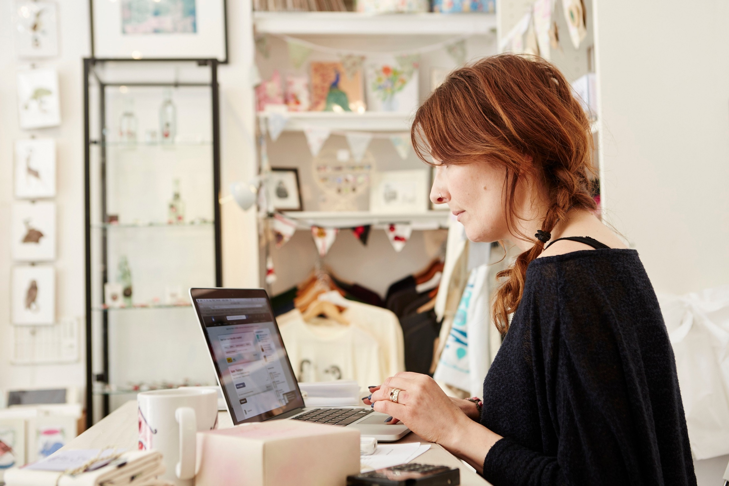 A woman in a small crafts supplier and gift shop, using a laptop, working,